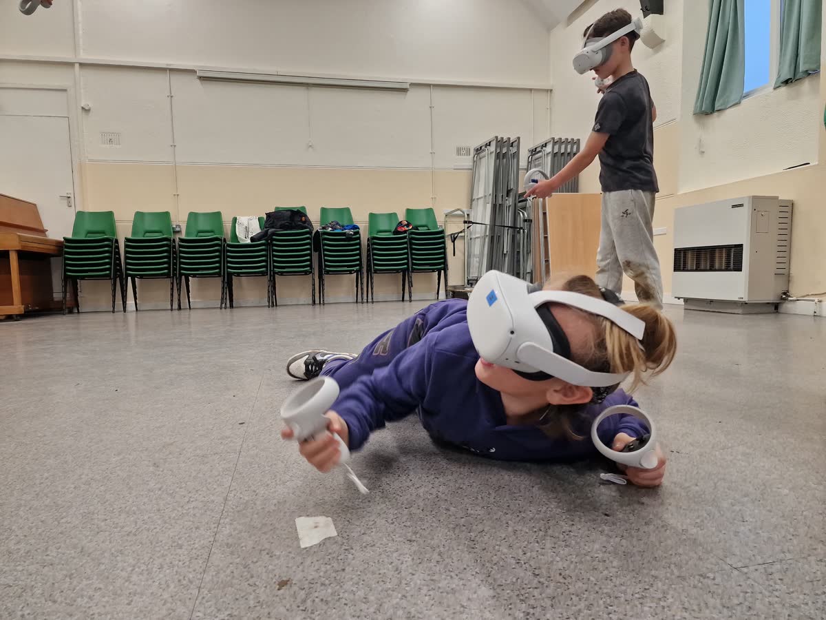 A young player in a VR headset diving across the floor mid-game